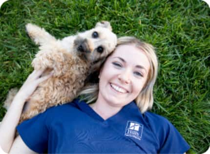 Un perro pequeño acostado en el césped junto a una investigadora de Hill's