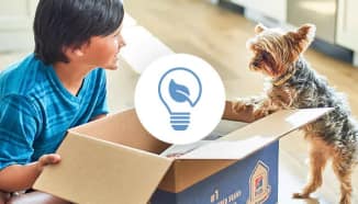  Un niño pequeño y un perro mirando una caja reciclable de Hill’s con un ícono de reducción de desperdicios